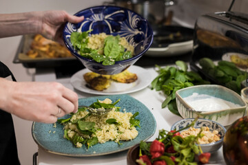 Close up of woman hands garnishing a fresh vegetarian salad with cous cous. Woman cooking in the kitchen at home preparing healthy food. Mediterranean cusine concept.