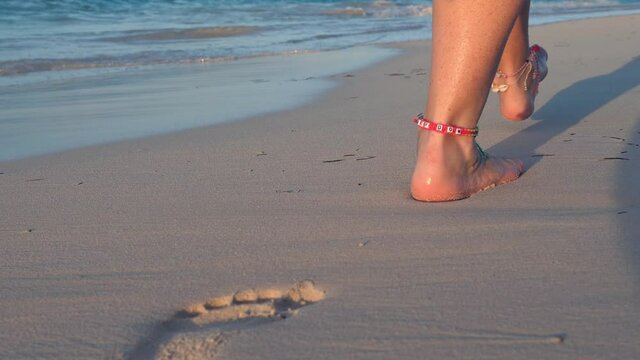Woman legs, walking along the beach. Leaving footprints on sand
