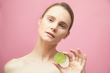 Beautiful sensual topless brunette woman standing isolated over pink background and hold lime in hand