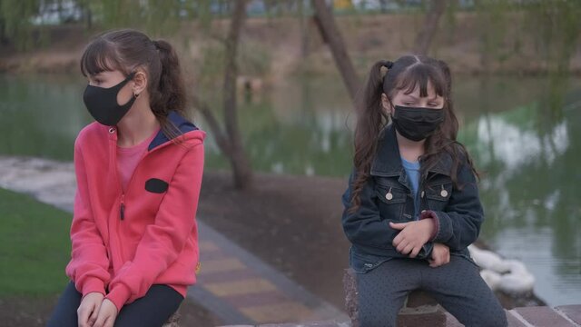 Children speak in quarantine. A view of two sisters bothe in protective mask speak with eath other in the park by the water in quarantine.