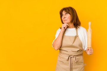 Middle age caucasian cook woman holding a roller isolated looking sideways with doubtful and skeptical expression.