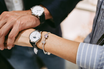 Beautiful couple enjoying in shopping at modern jewelry store. Close up shot of human hand holding expensive watch. - obrazy, fototapety, plakaty