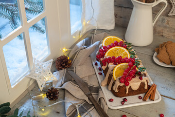 Traditional christmas cinnamon cake decorated with fruits and spekulatius cookies cream on a kitchen countertop.
