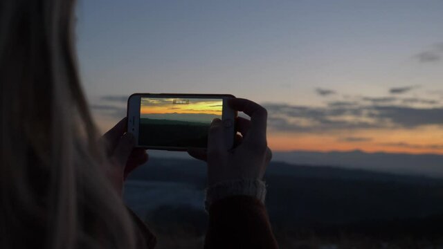 Sudetes, Poland - 01 December 2020: Woman with iPhone record video of mountains in sunset time