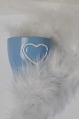 Small blue cup with heart in feathers on white background.