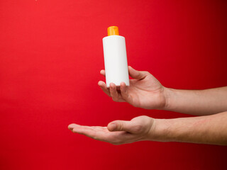 Hand holding white shampoo bottle isolated on red background.