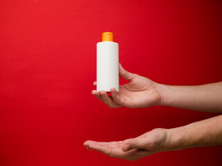 Hand holding white shampoo bottle isolated on red background.