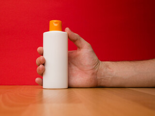 Hand holding white shampoo bottle isolated on red background.