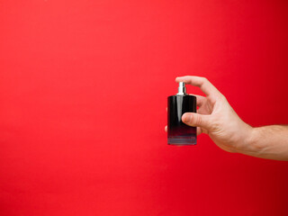 Hand of European men holding perfume. Isolated on red background. Studio portrait.