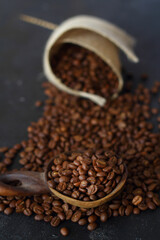 Fresh roasted arabica coffee beans in a wooden spoon and scattered coffee beans on a wooden table.