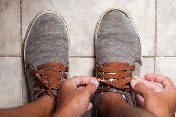 Detail of the hands of a young Brazilian man tying the tennis shoe to practice walking in the neighborhood. Footwear concept. Sport concept.