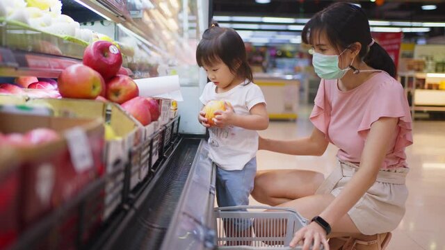 Asian young mother wearing face mask while choosing apple with her kid