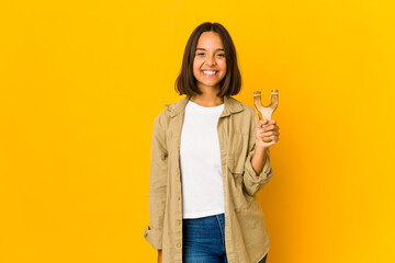 Young hispanic woman holding a slingshot happy, smiling and cheerful.