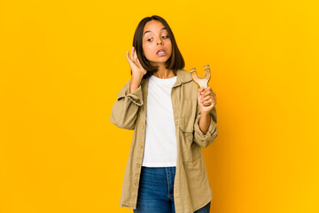 Young hispanic woman holding a slingshot trying to listening a gossip.