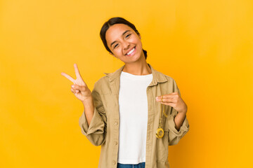 Young hispanic woman holding a pocket watch joyful and carefree showing a peace symbol with fingers.