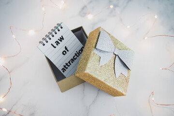 law of attraction, text on notepad inside of present box surrounded by fairy lights