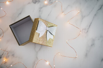 presents and special occasions, open gift box with gold and silver glitters surrounded by fairy lights on marble desk