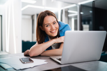 Smiling woman sitting in the kitchen and using the laptop. Working from home in quarantine lockdown. Social distancing Self Isolation.