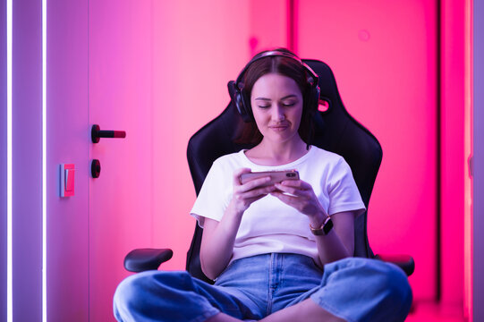 Cybersport gamer playing mobile game on the smart phone sitting on a gaming chair in neon color room.