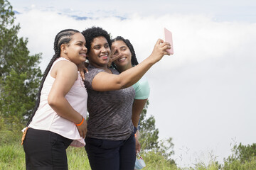three happy hispanic young girls outdoor enjoying the nature during a vacation trip smiling taking selfie photography in a summer day in dominican republic - obrazy, fototapety, plakaty