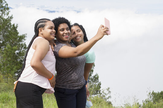 three happy hispanic young girls outdoor enjoying the nature during a vacation trip smiling taking selfie photography in a summer day in dominican republic