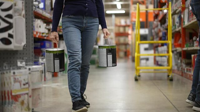 Slow motion of woman holding two cans of paint walking aisle in hardware store. Concept of coronavirus shopping experience.