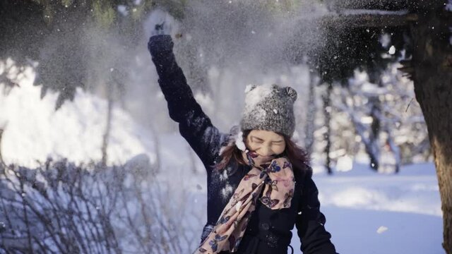 Happy young woman pulling the snowy branch of tree over her head. Winter, sport, holidays, relationship, love, xmas, lifestyle concept. Filmed on cinema camera, 10 bit color space.
