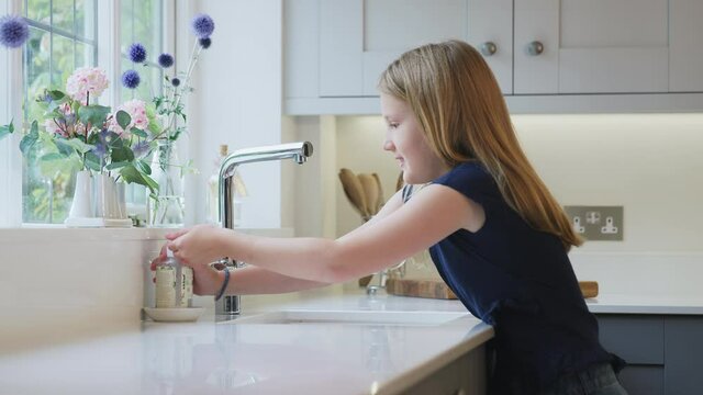 Girl walks into frame then turns on tap and washes hands in kitchen sink to prevent transmission of virus during health pandemic - shot in slow motion