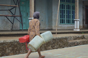 a mother is walking while carrying a jerry can filled with water in a village. The village experienced water shortages due to the long drought