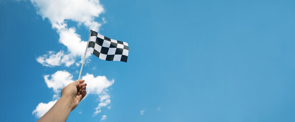 checkered race flag in hand over blue sky