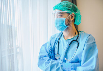 Asian male doctor wearing medical gown with face shield and mask before working in operating room in hospital.