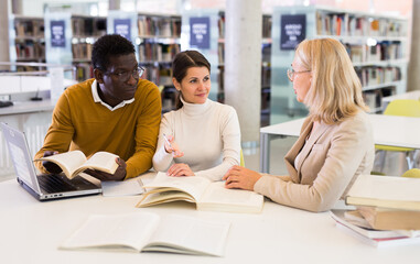 Female tutor helping students preparing for exam in library. High quality photo