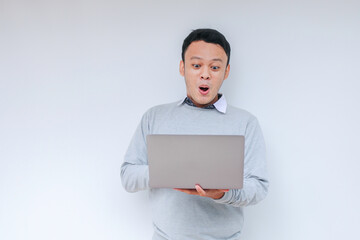 Wow face of Young Asian man shocked what he see in the laptop when working isolated grey background wearing grey shirt