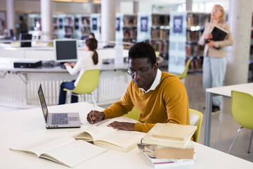 Confident african-american man working on laptop in public library. High quality photo