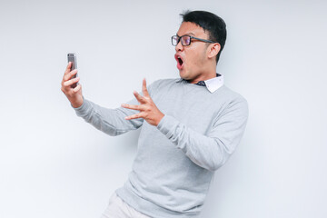 Wow face of Your Asian man shocked what he see in the smartphone on isolated grey background.