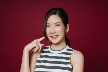 Portrait of beautiful asian woman pointing at her cheeks isolate on red background.