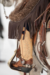 Fototapeta na wymiar Young cowboy boot close up leather with fringed chaps close cropped young boy in saddle in winter western attire and tack 