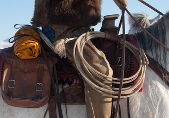 cowboys lasso coiled up and hanging on western saddle against suede western chinks or chaps saddle bags attached to saddle