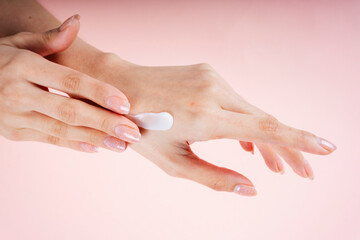 Hand of woman applying lotion cream isolate on pink background.