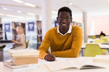 Fototapeta na wymiar Portrait of happy african-american male student working with book in public library. High quality photo
