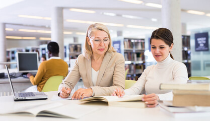 Obraz premium Female teacher working with girl student in university library. High quality photo