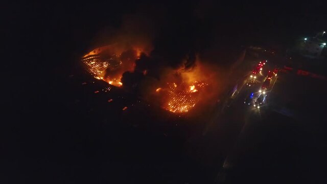 Aerial view of firetrucks and firefighters trying to save a building on fire, night, in Australia - static, drone shot