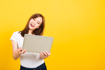 Fototapeta na wymiar Asian happy portrait beautiful cute young woman teen smile standing wear t-shirt hold laptop computer and excited celebrating success looking to camera, studio shot yellow background with copy space