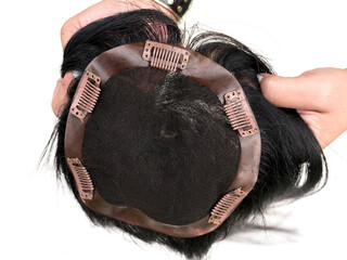 Holding a hair toupee or topper exposing the inside and showing the clips to help secure the...