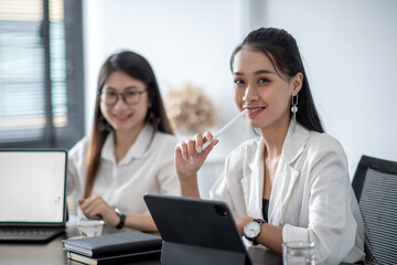 Obraz premium Young asian business woman meeting to work and using digital tablet with their colleagues in the office. Looking at camera.