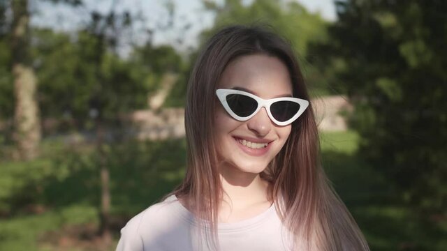Beautiful young woman with sunglasses showing OK outdoors