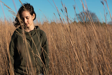 mujer joven parada en medio de un campo de trigo mirando hacia abajo pensativa - obrazy, fototapety, plakaty