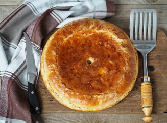 Round large pie with filling on a napkin on an ancient wooden background. Festive or casual homemade baked goods.