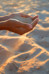 Young woman holds sand in her hands, at sunset