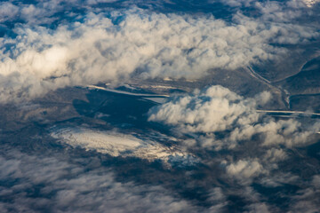 Snowy mountains from a bird's eye view on a clear blue sky with clouds.
